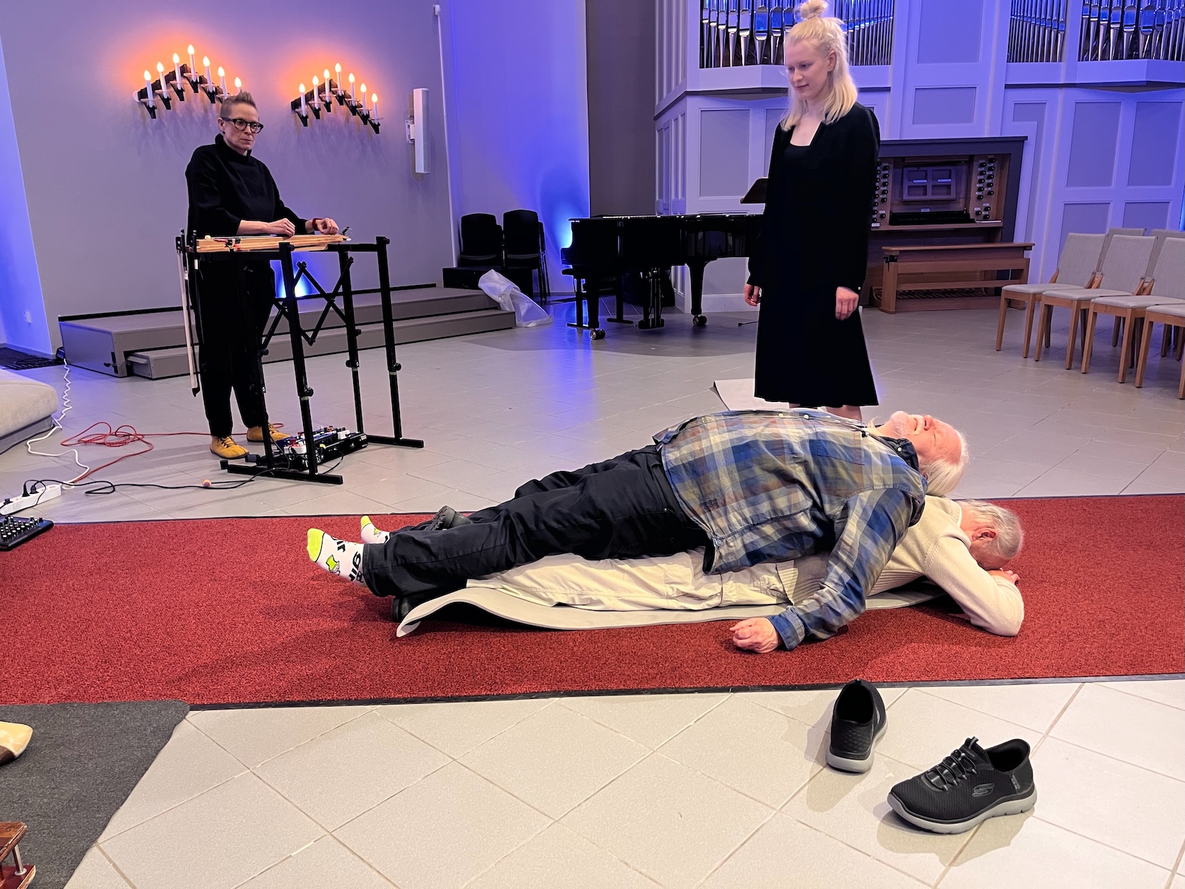 TRAINING FOR DEATH, Pispala Church, Tampere, Finland, 2025. Marja Rautakorpi instructing a couple of participants, Pauliina Kauppila playing music.